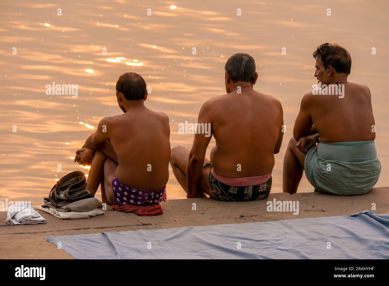 Varanasi, Indien - 14. November 2015. Drei südasiatische Männer mittleren Alters sitzen auf einem GHat am Ganges River bei Sonnenaufgang, angezogen zum Baden, während Diwali. Stockfoto