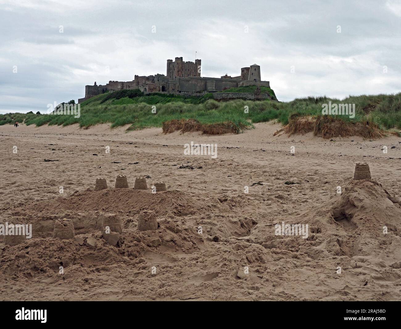 Mächtige Festung von Bamburgh Castle, die über Sanddünen und Nordseestrand thront, mit blassen nachgeahmten Sandburgen in Northumbria, England, Großbritannien Stockfoto