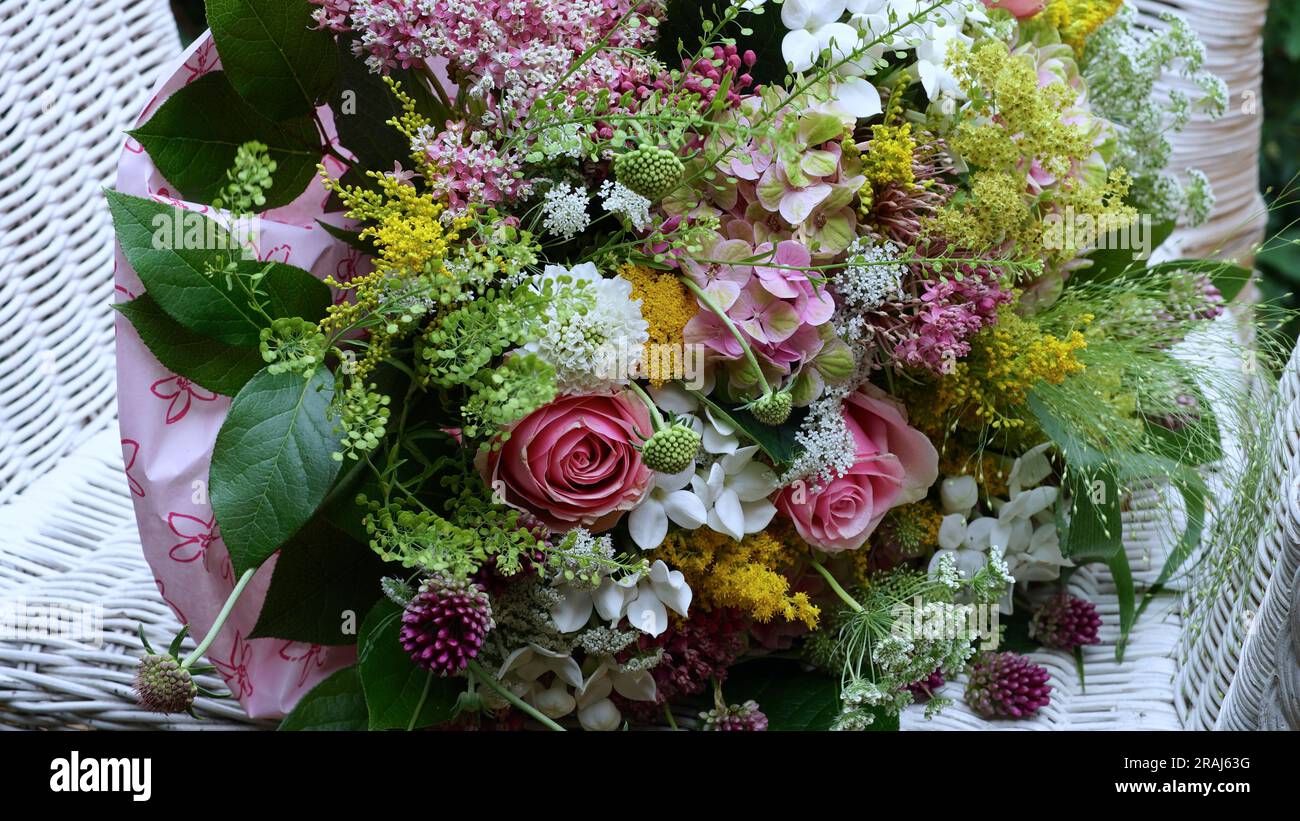 Ein Strauß wunderschöner Sommerblumen. Pastellfarben. Er lag auf einem weißen Korbstuhl. Stockfoto