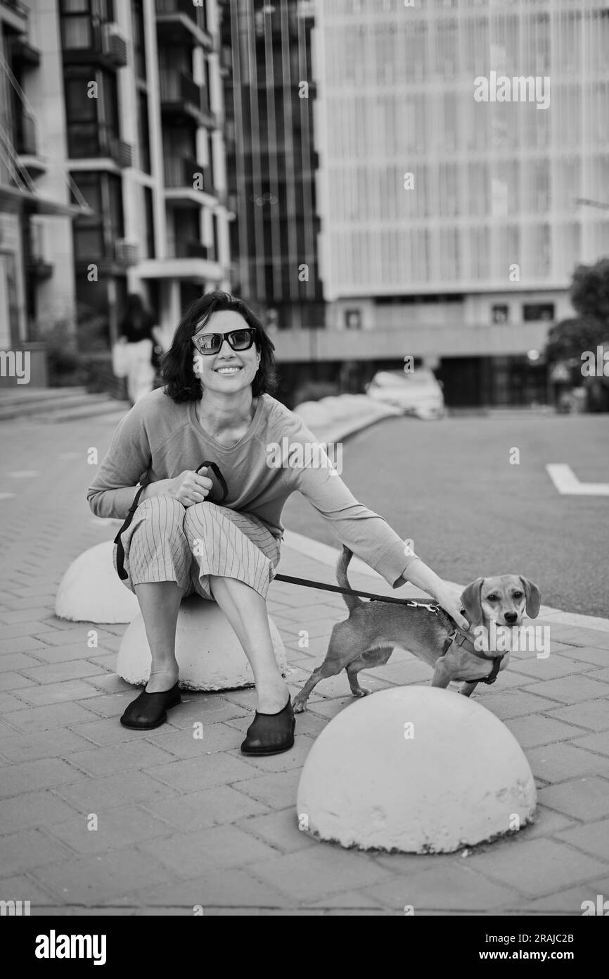 Junge, hübsche Erwachsene Frau mit einem kleinen Ingwerhund, die in der Stadt spazieren geht und Spaß hat. Blick auf die Stadt Foto in hoher Qualität Stockfoto