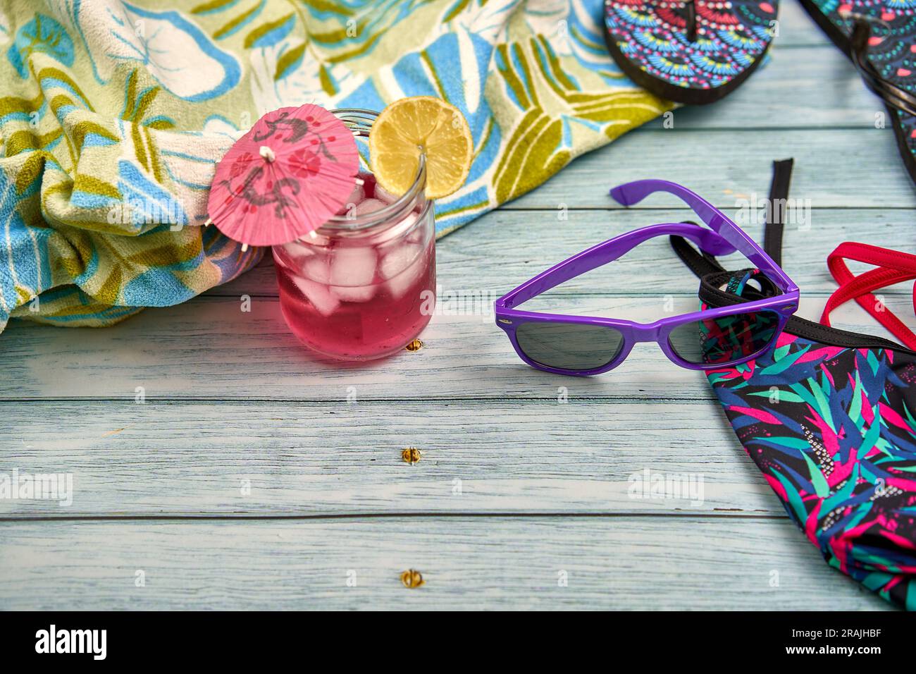 Wassermelone und Zitronengetränk, violette Sonnenbrille, Flip Flops, Bikini und ein Strandtuch mit tropischem Muster auf einem Holztisch. Stockfoto