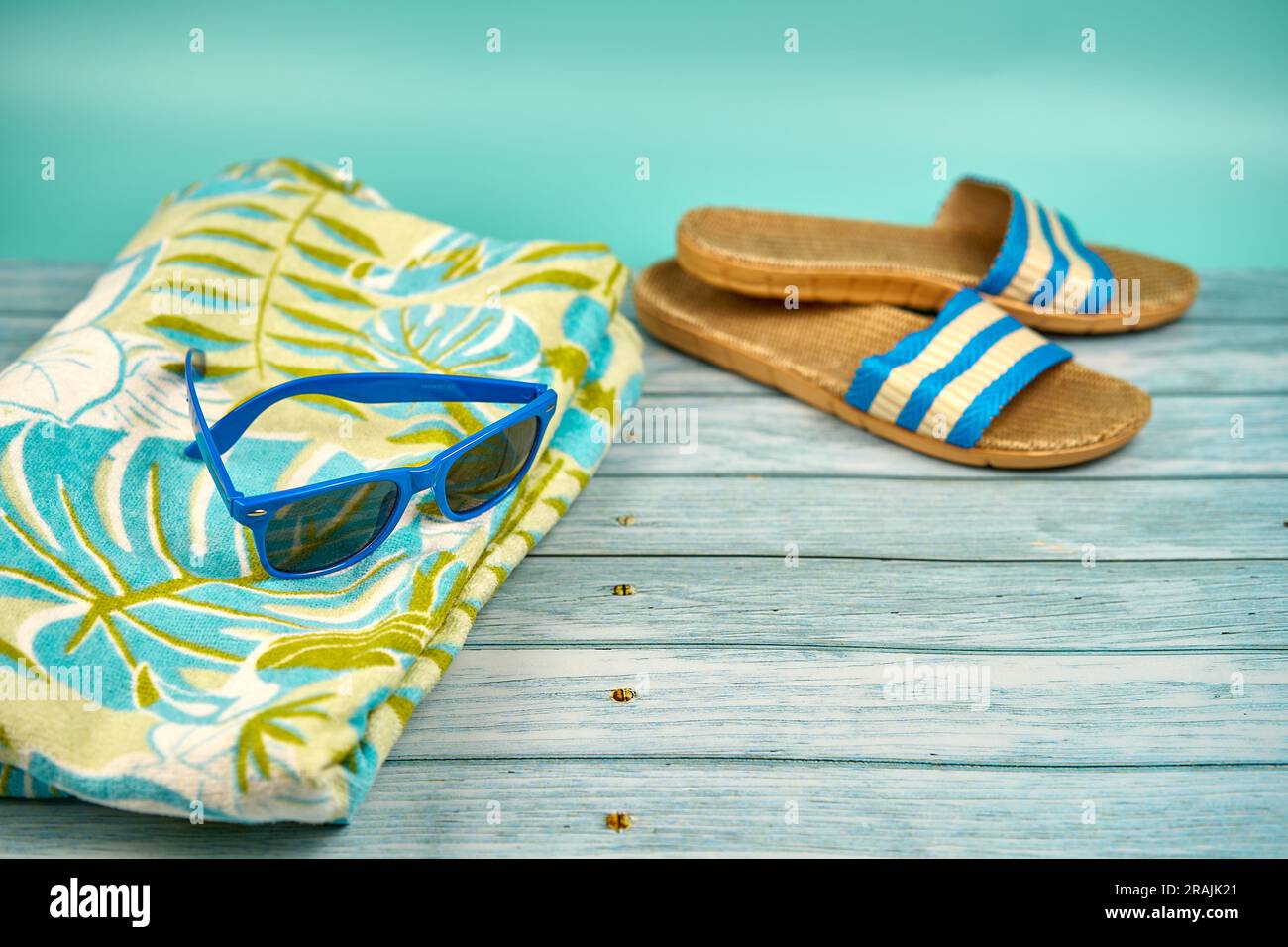 Blaue Sonnenbrille, Sandalen und Strandtuch, auf einem Holztisch und grünem Hintergrund. Stockfoto
