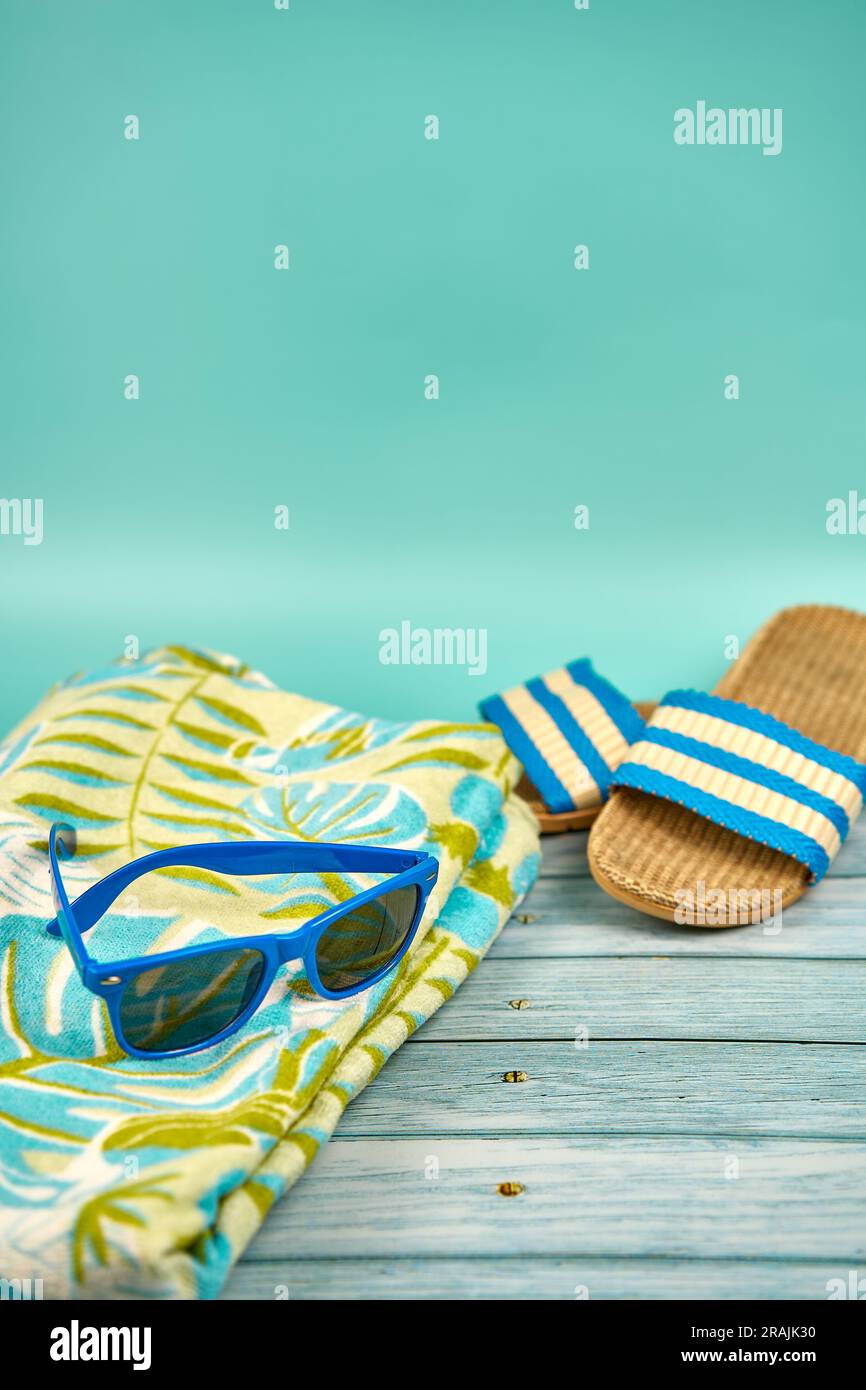 Sommerstille, bestehend aus blauer Sonnenbrille, Sandalen und Strandtuch, auf einem Holztisch und grünem Hintergrund. Stockfoto