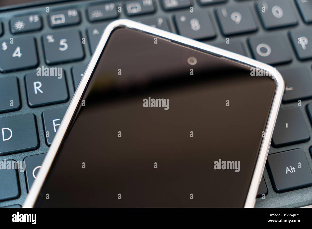 Ein leerer Bildschirm auf einem Smartphone, das auf einer schwarzen Laptop-Tastatur liegt. Blick von oben. Speicherplatz kopieren Stockfoto