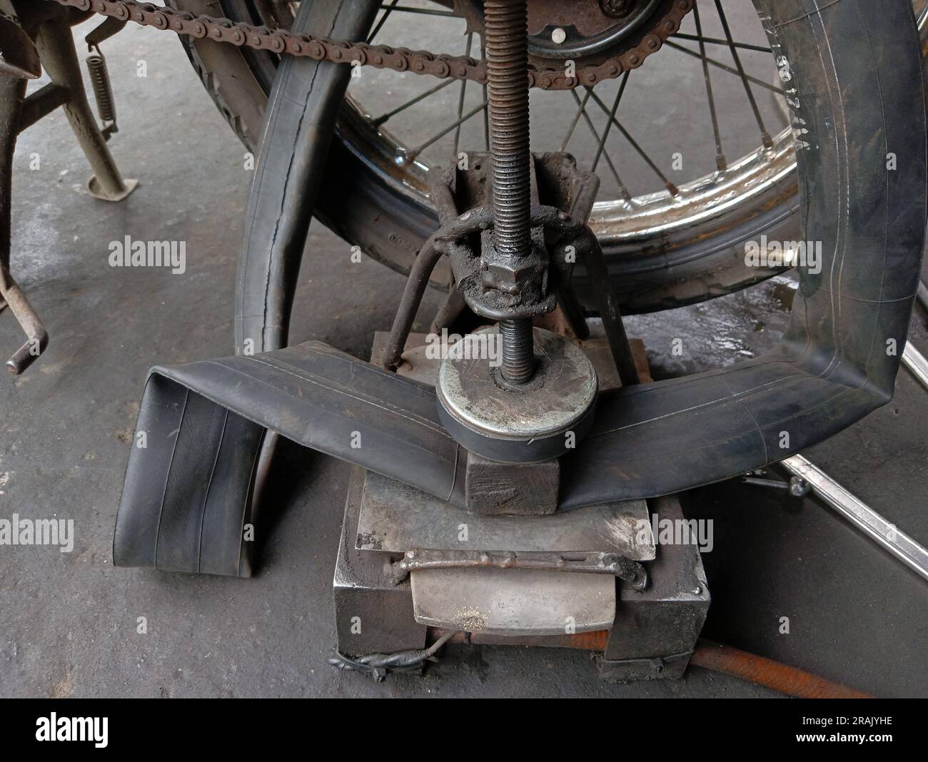 Ein Motorrad, dessen Hinterreifen in einer Reparaturwerkstatt durchstochen und mit herkömmlicher Ausrüstung zum Ausbessern von Reifen aufgebessert wird. Stockfoto