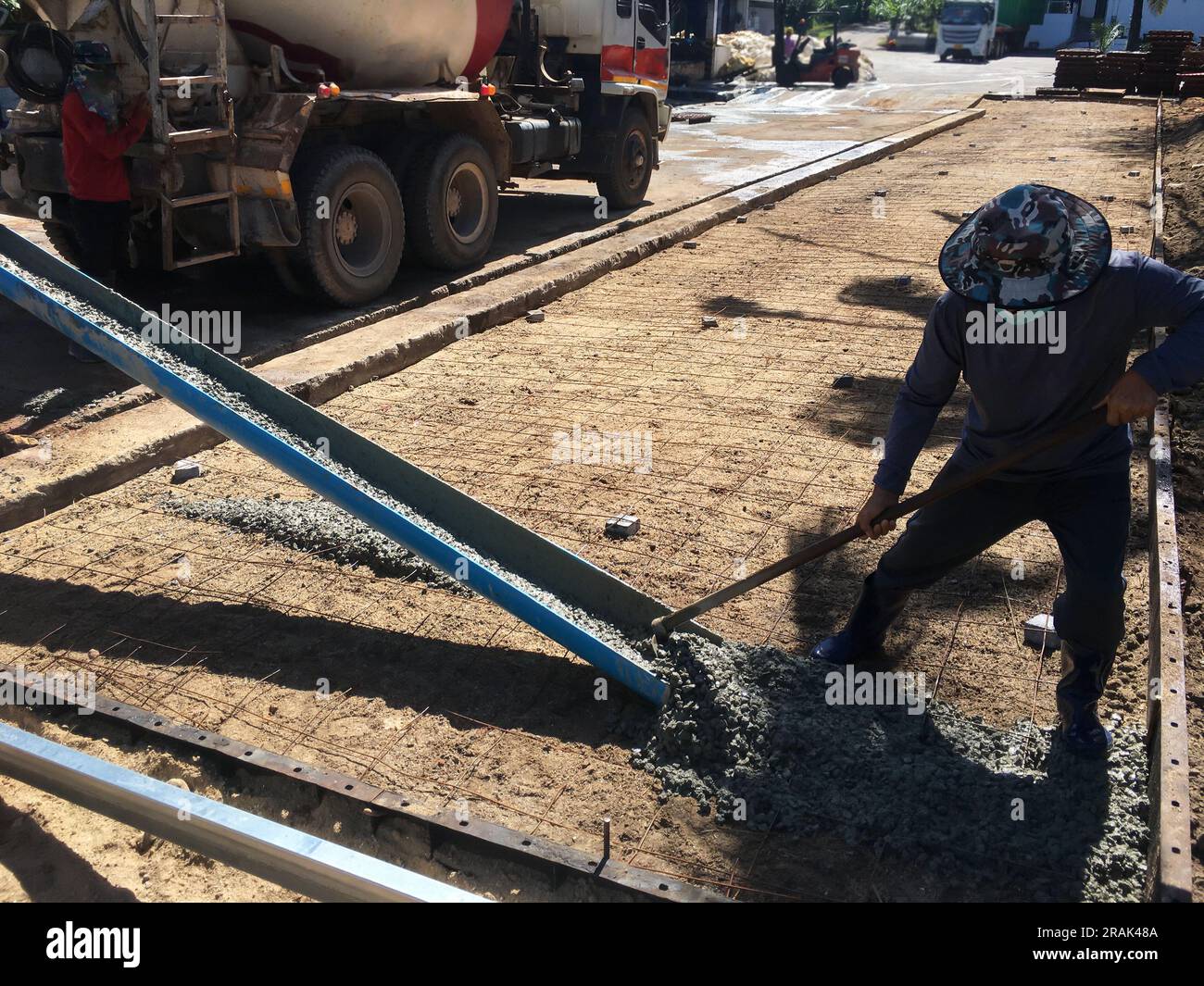 Arbeiter entladen Zement aus LKWs und verteilen ihn im gesamten Bereich. Dabei wird Zement gegossen, um eine Betonstraße zu schaffen. Stockfoto
