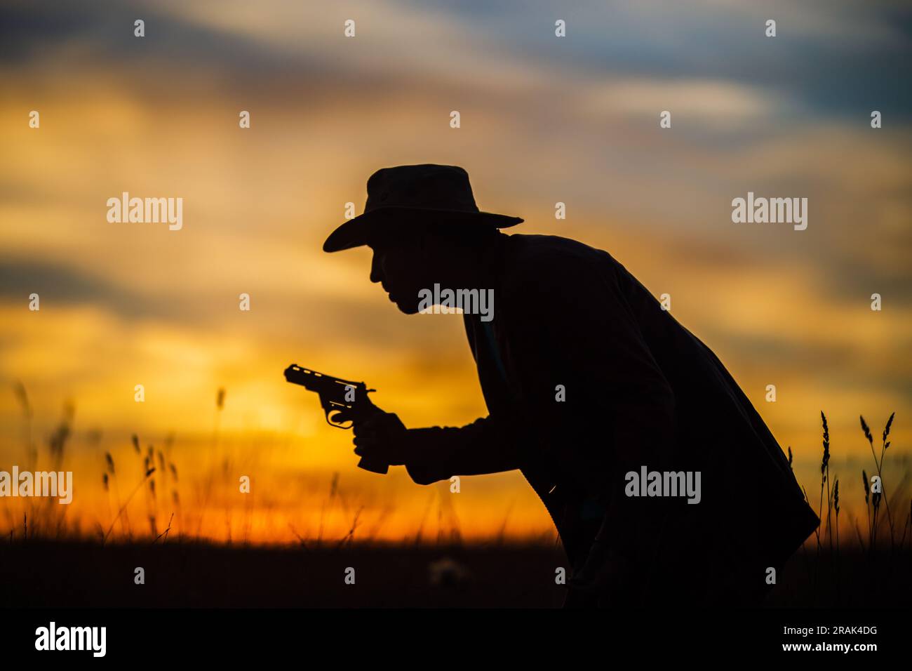 Silhouette eines Cowboys in einem Hut mit einem Revolver gegen einen dramatischen Sonnenuntergang Himmel. WESTERN-Konzept. Leben im wilden Westen Stockfoto