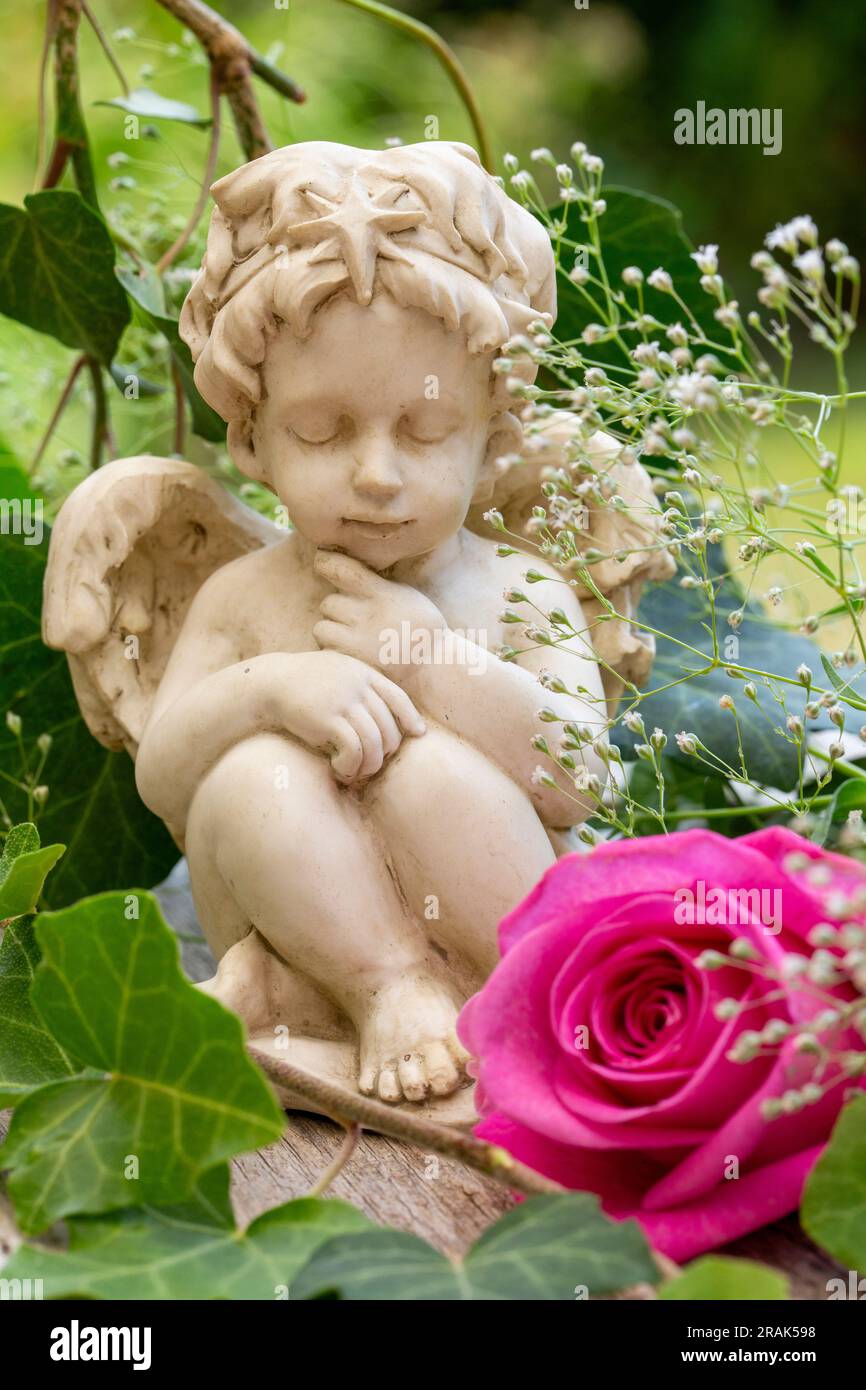 Kleine Engelsfigur mit rosa Rosen und grünen Blättern in einem Garten Stockfoto