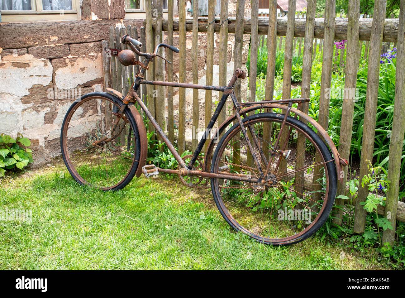 Altes rostiges beschädigtes Fahrrad, das sich an einen Holzzaun in einem ländlichen Gebiet lehnt Stockfoto