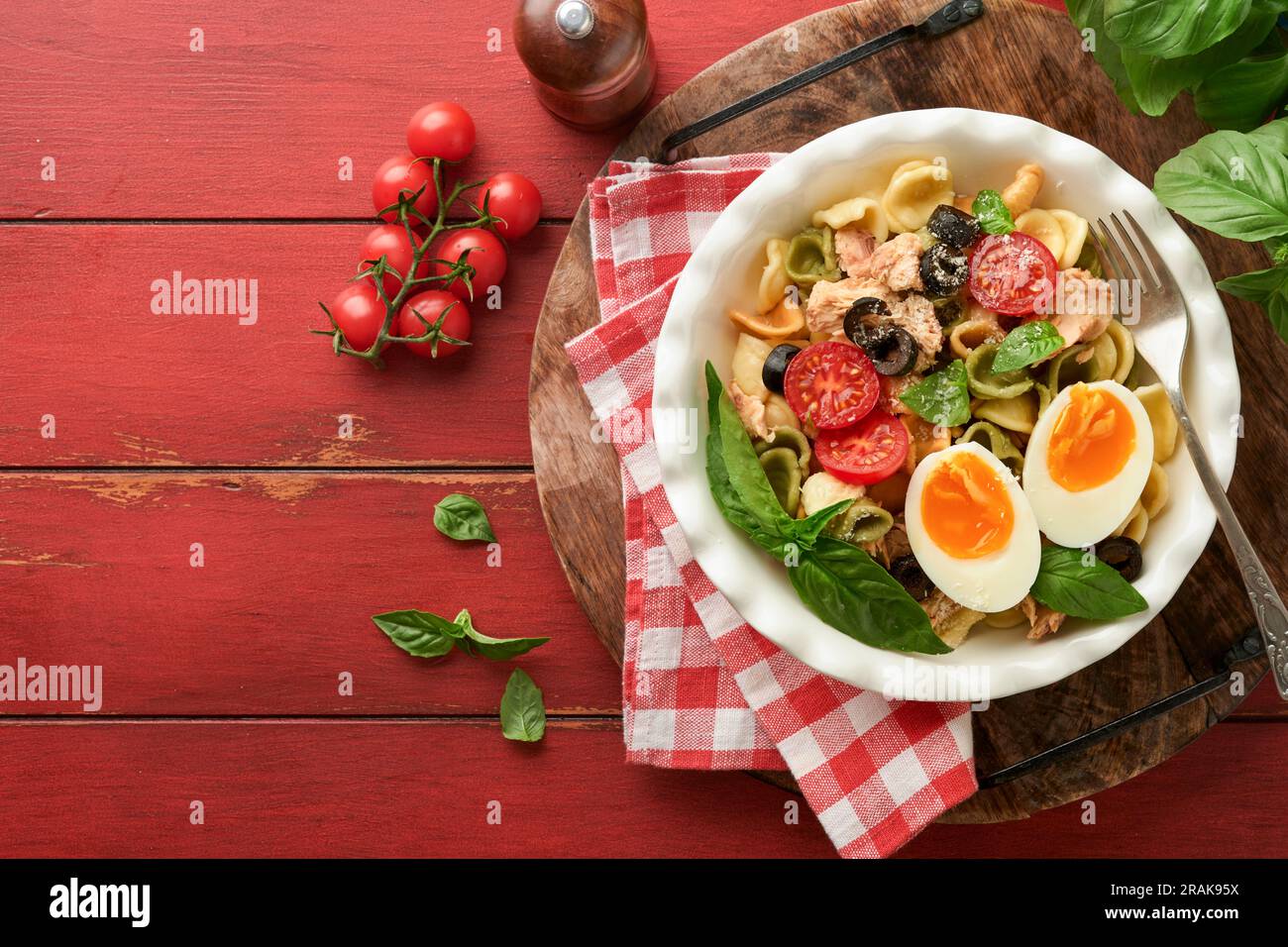 Italienischer Nudelsalat. Orekchiette Pasta mit Thunfisch, Tomatenkirsche, Oliven, Basilikum und Parmesan auf einem roten, alten rustikalen Tischhintergrund. Traditi Stockfoto