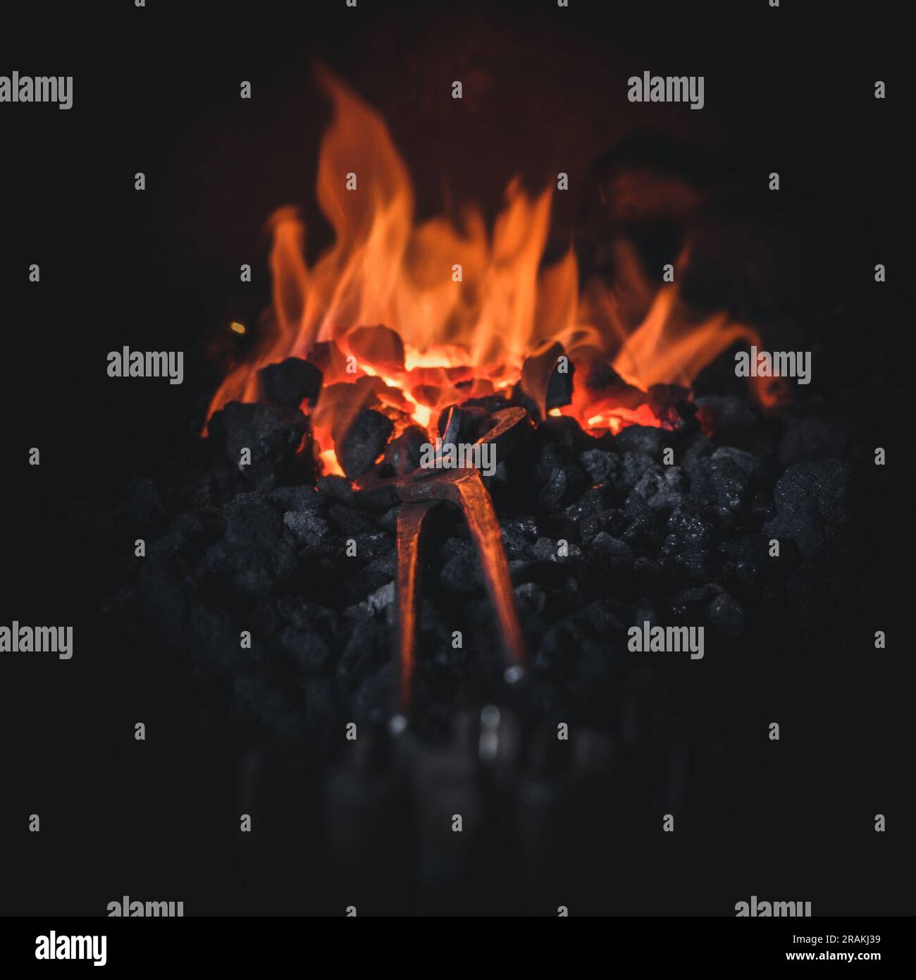 Schmied schmiedet mit Flammen auf heißen Kohlen und Werkzeugen im Feuer, um Metallkunst und Artefakte zu erschaffen Stockfoto