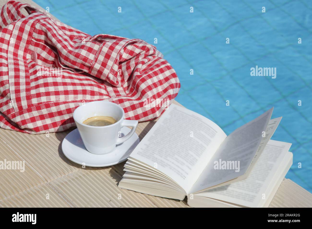 Offenes Buch und eine Tasse Kaffee neben dem Swimmingpool. Freizeitkonzept für Sommertage Stockfoto
