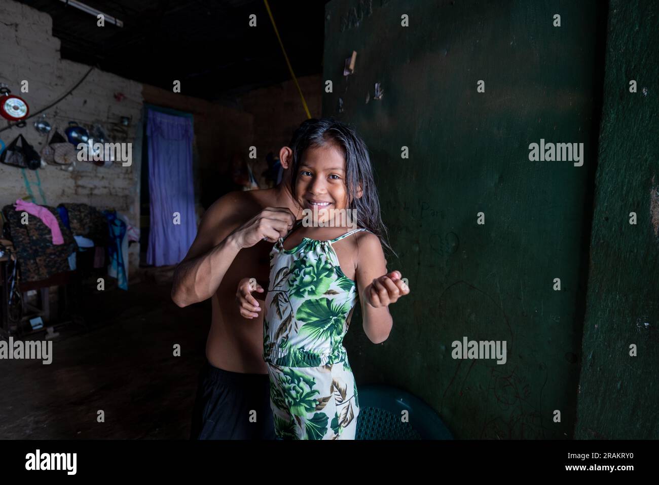 Ahuachapán, El Salvador - November 04 2022: Little Salvadoran Girl lächelt und schaut in die Kamera, während ihr Bruder ihr beim Anziehen hilft Stockfoto