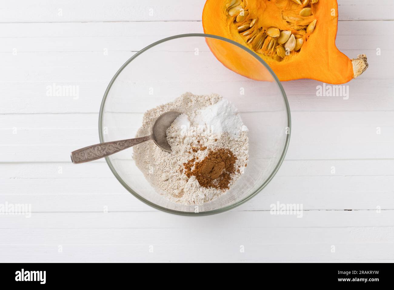 Glasschüssel mit Hafermehl, Backpulver und gemahlenem Zimt, halber Kürbis mit Samen auf weißem Holzhintergrund, Draufsicht. Stufe des Kochens d Stockfoto