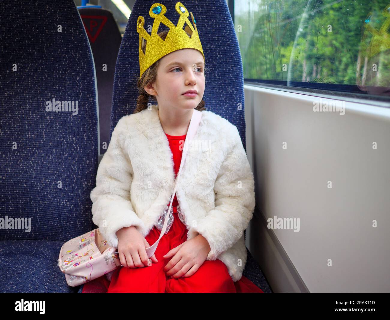 Ein Mädchen mit Spielzeugkrone, das mit dem Zug zu einer Veranstaltung in England reist Stockfoto