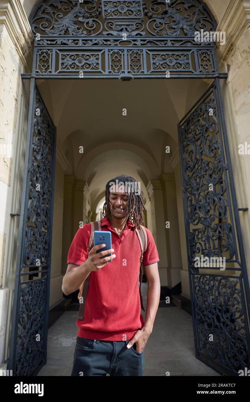 Männlicher Student, der Nachrichten oder soziale Medien auf einem Mobiltelefon außerhalb des Universitätsgebäudes in Oxford UK abfragt Stockfoto