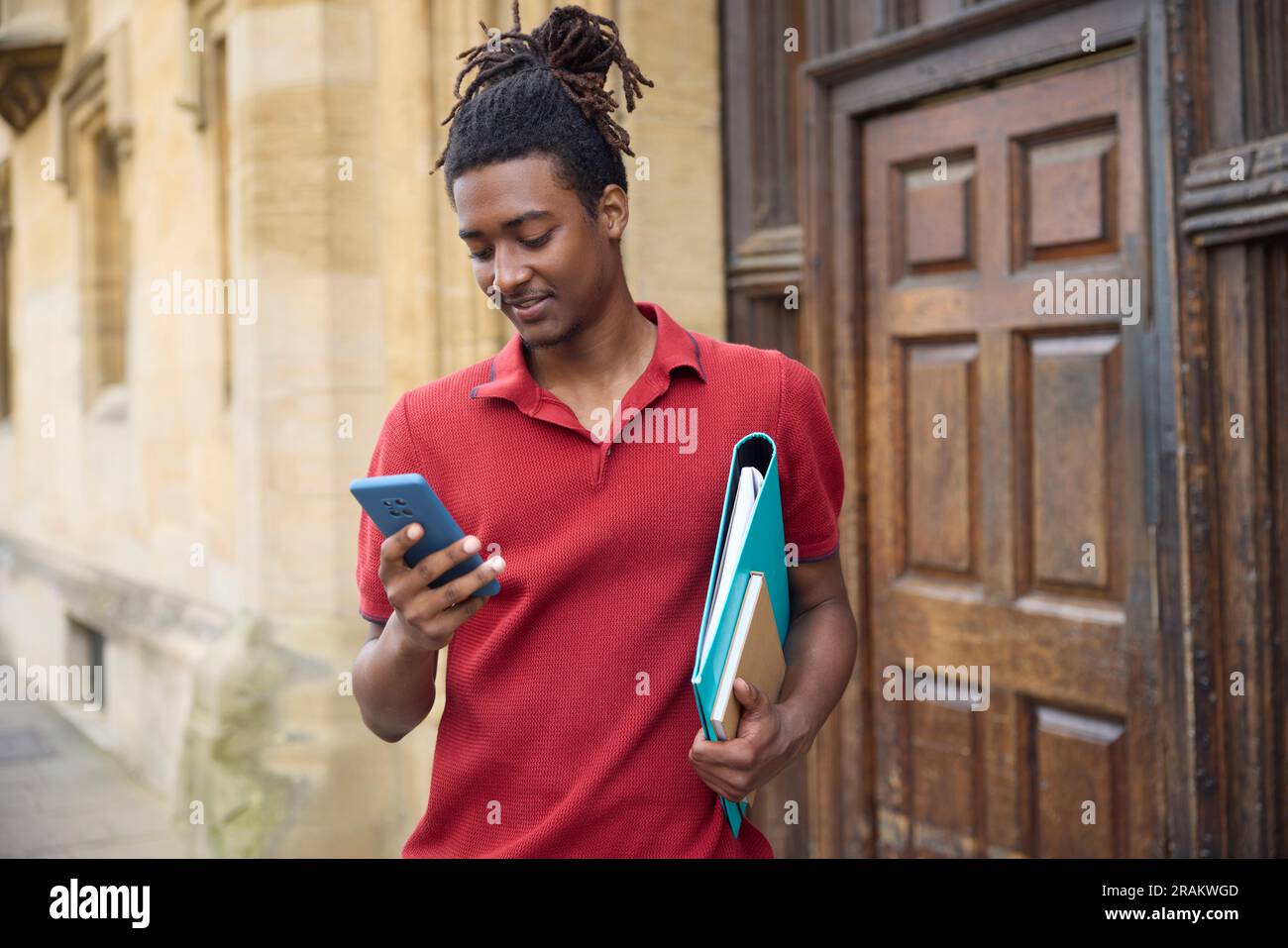 Männlicher Student, der Nachrichten oder soziale Medien auf einem Mobiltelefon außerhalb des Universitätsgebäudes in Oxford UK abfragt Stockfoto