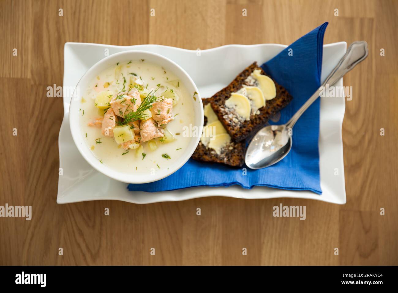 Eine Schüssel finnische Lohikeitto-Suppe, serviert auf einem Holztisch mit einem Stück schwedischem Roggenbrot. Cremige Brühe, zarte Kartoffeln und fleckiger rosa Lachs Stockfoto