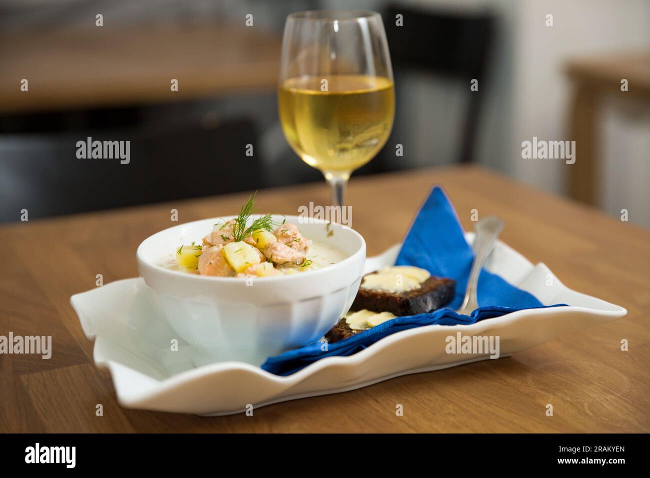 Eine Schüssel finnische Lohikeitto-Suppe, serviert auf einem Holztisch mit einem Stück schwedischem Roggenbrot. Cremige Brühe, zarte Kartoffeln und fleckiger rosa Lachs Stockfoto