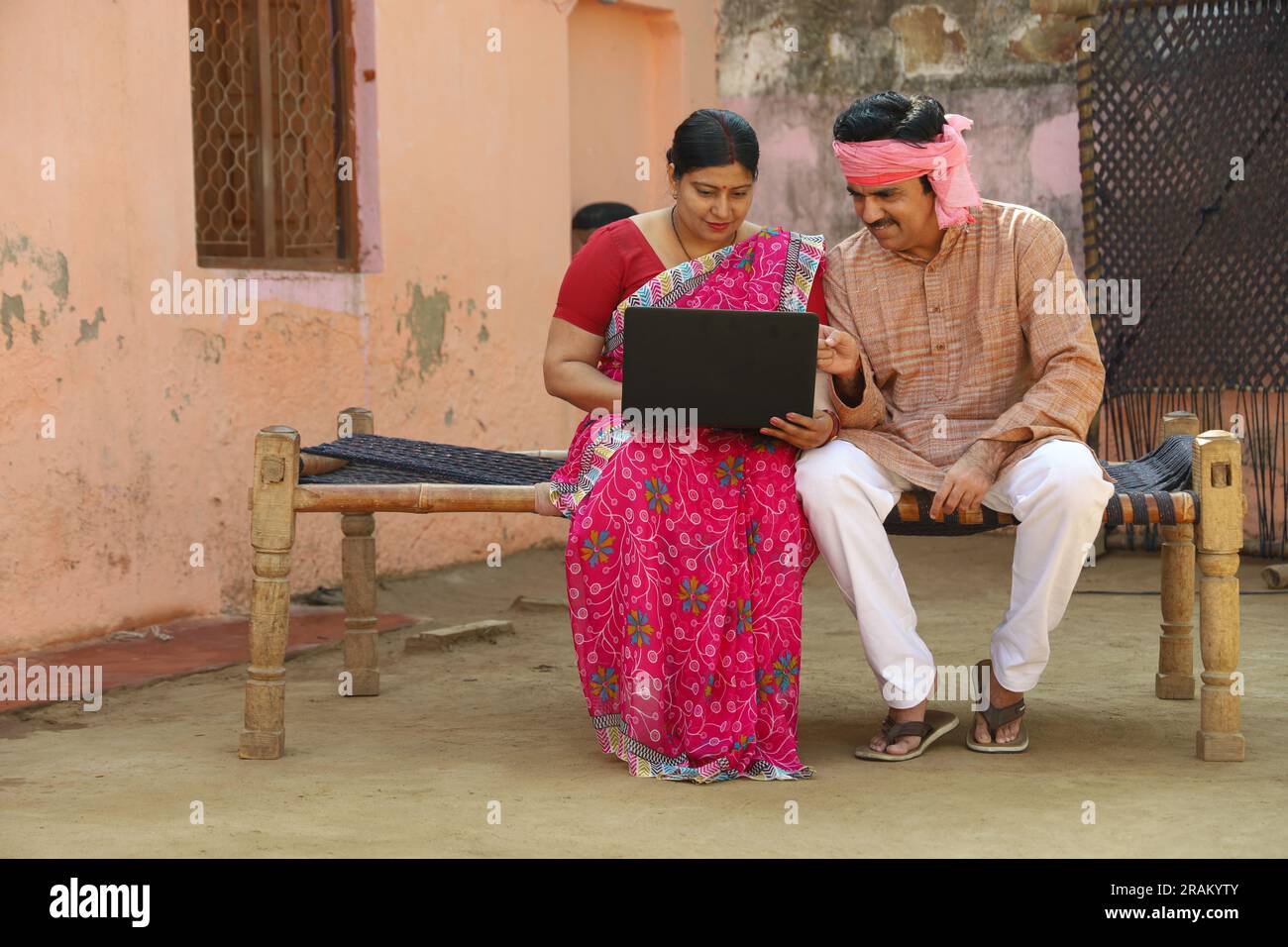 Mann und Frau zahlen gerne online. Ländliches indisches Paar, das mit Kreditkarte bezahlt. Ein Paar, das auf einem Kinderbett im Flur sitzt. Stockfoto