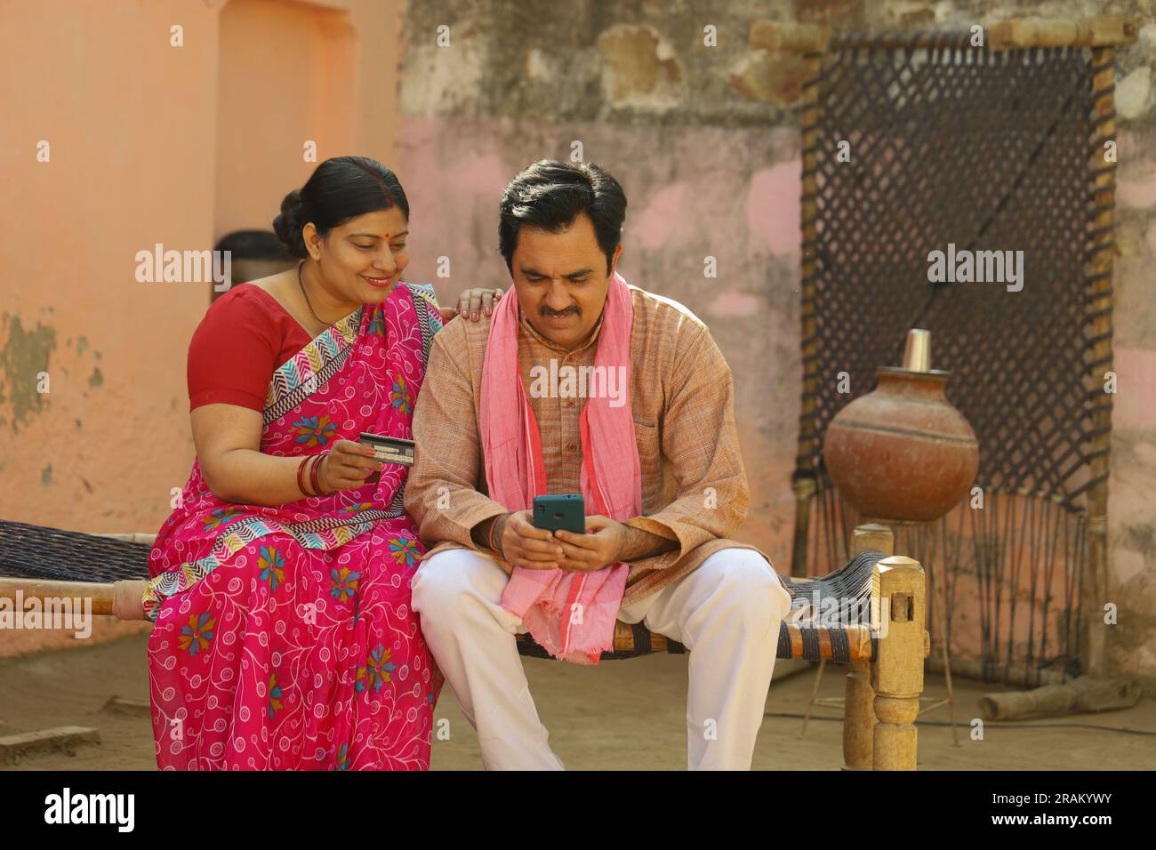 Eine glückliche Familie aus dem indischen Dorf, die den Laptop vor dem Haus benutzt hat. Mann und Frau zahlen gerne online mit Kreditkarte Stockfoto