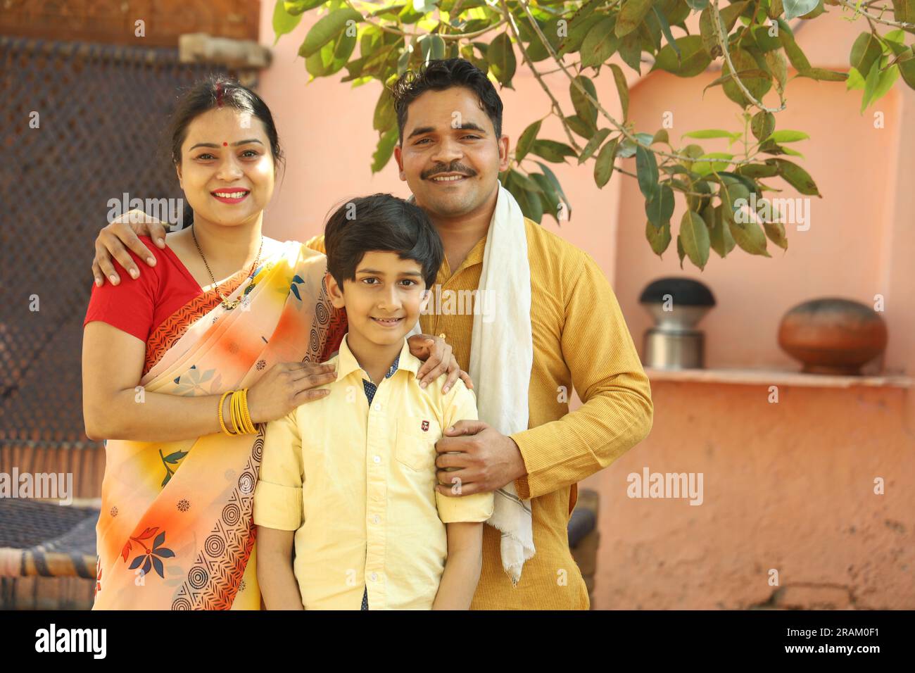 Porträt einer indischen Bauernfamilie von Vater, Mutter und Sohn, die zusammen auf einem Kinderbett in indischer Dorfkleidung sitzen. Stockfoto