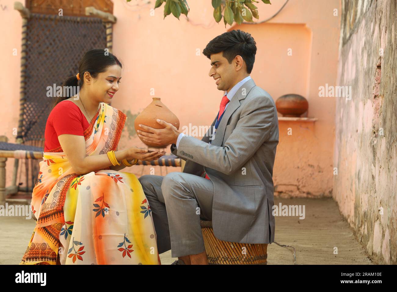 Glückliche ländliche indische Frauen, die mit einer Versicherungsagentin sitzen, die die Piggy Bank hält. Eine Frau, die sich freut, dass ihr Geld gespart wurde. Stockfoto