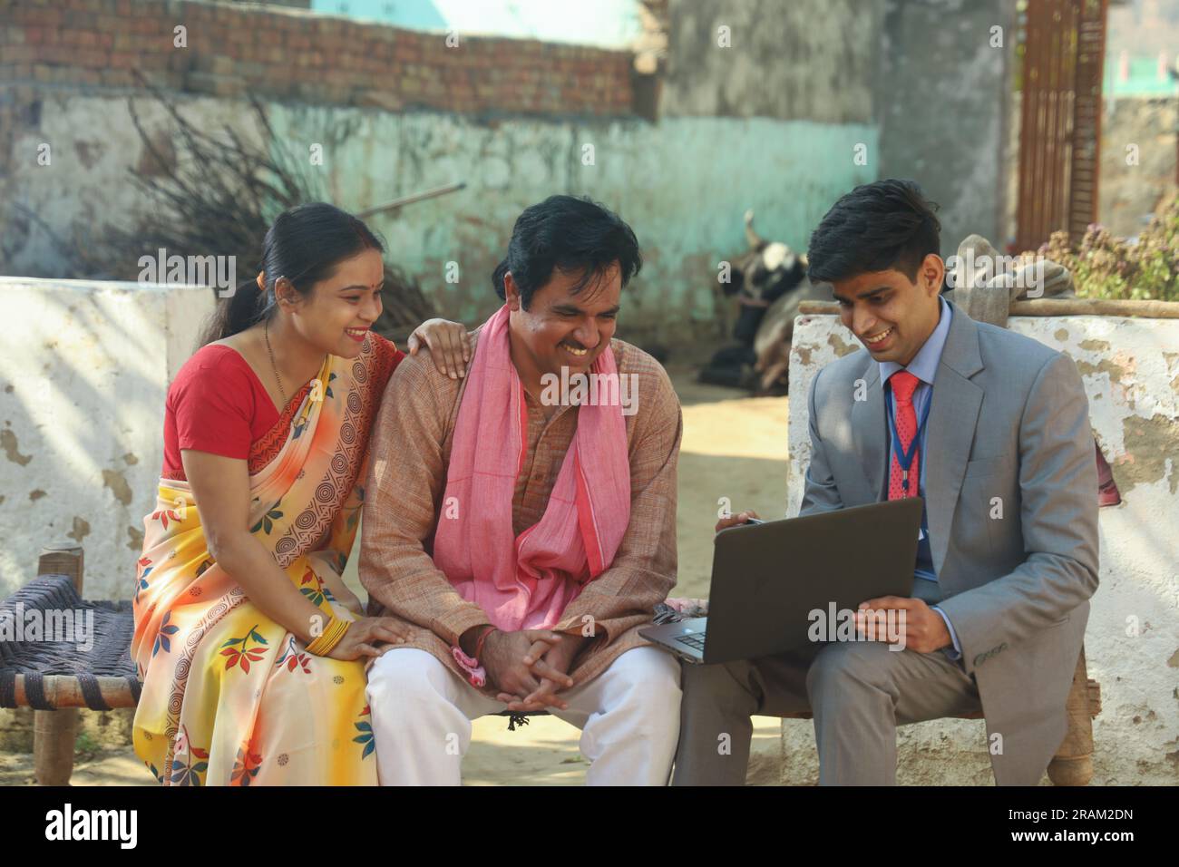 Glückliche Familie im indischen Dorf, die mit dem Banker oder Finanzberater saß und den Laptop vor dem Haus benutzte. Ausbildungsdarlehen Stockfoto