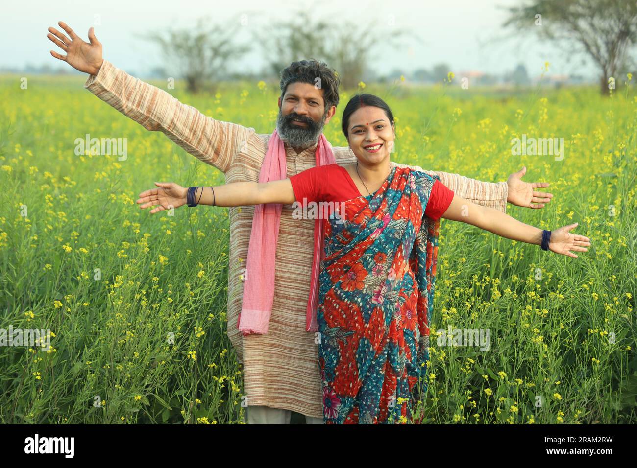 Glückliches indisches Bauernpaar, das auf dem Senffeld steht und die landwirtschaftlichen Profite genießt und froh ist, dass die gedeihten landwirtschaftlichen Ernten davon profitieren. Stockfoto