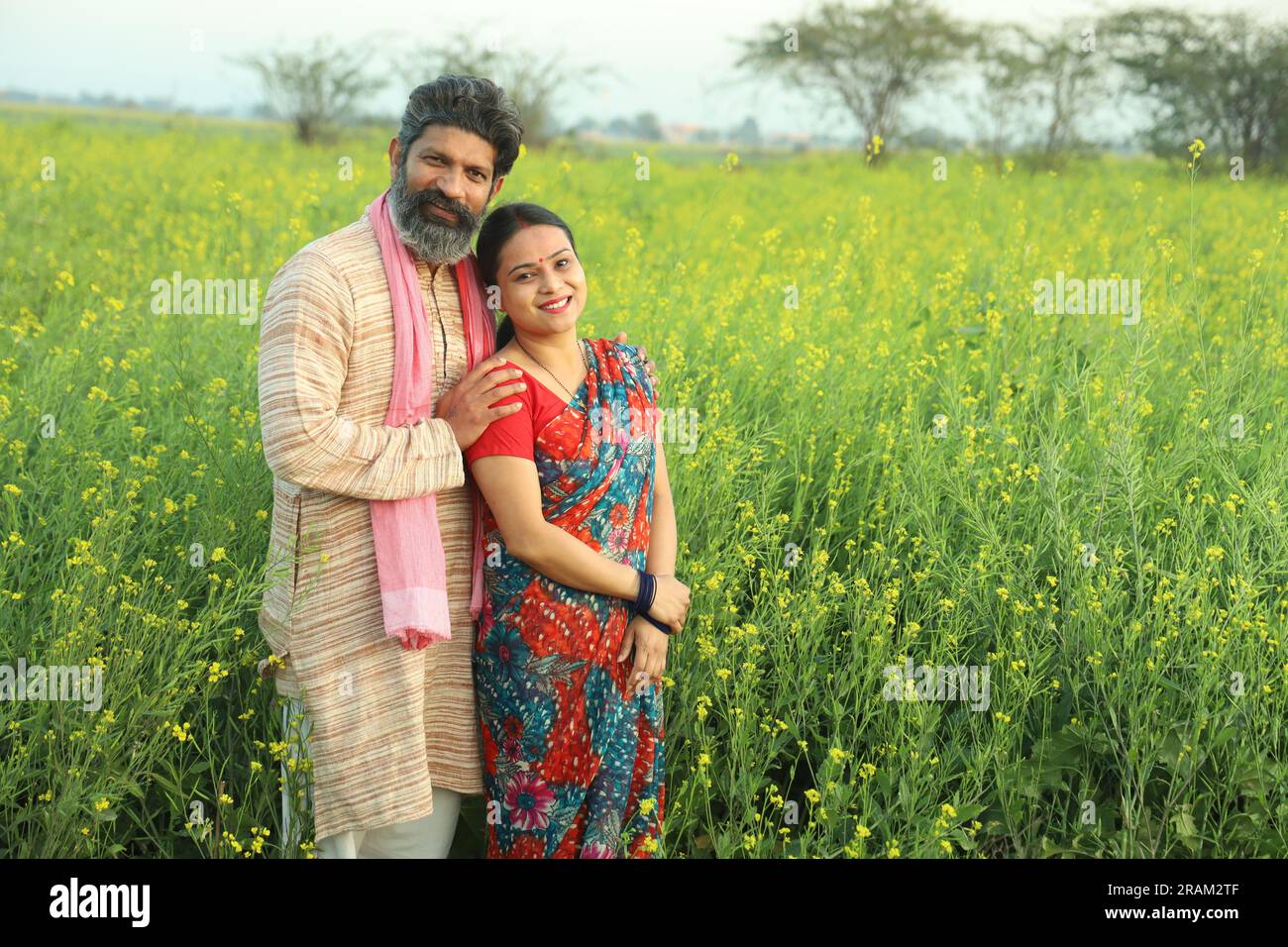 Glückliches indisches Bauernpaar, das auf dem Senffeld steht und die landwirtschaftlichen Profite genießt und froh ist, dass die gedeihten landwirtschaftlichen Ernten davon profitieren. Stockfoto