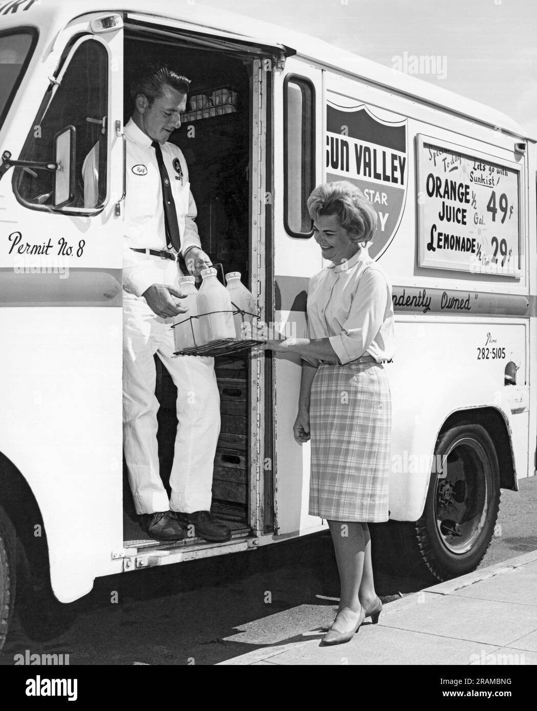 Kalifornien: ca. 1955 Eine Frau trifft den Milchmann von Sun Valley an seinem Truck, als er ankommt, um auf seiner Route eine Übergabe zu machen. Stockfoto