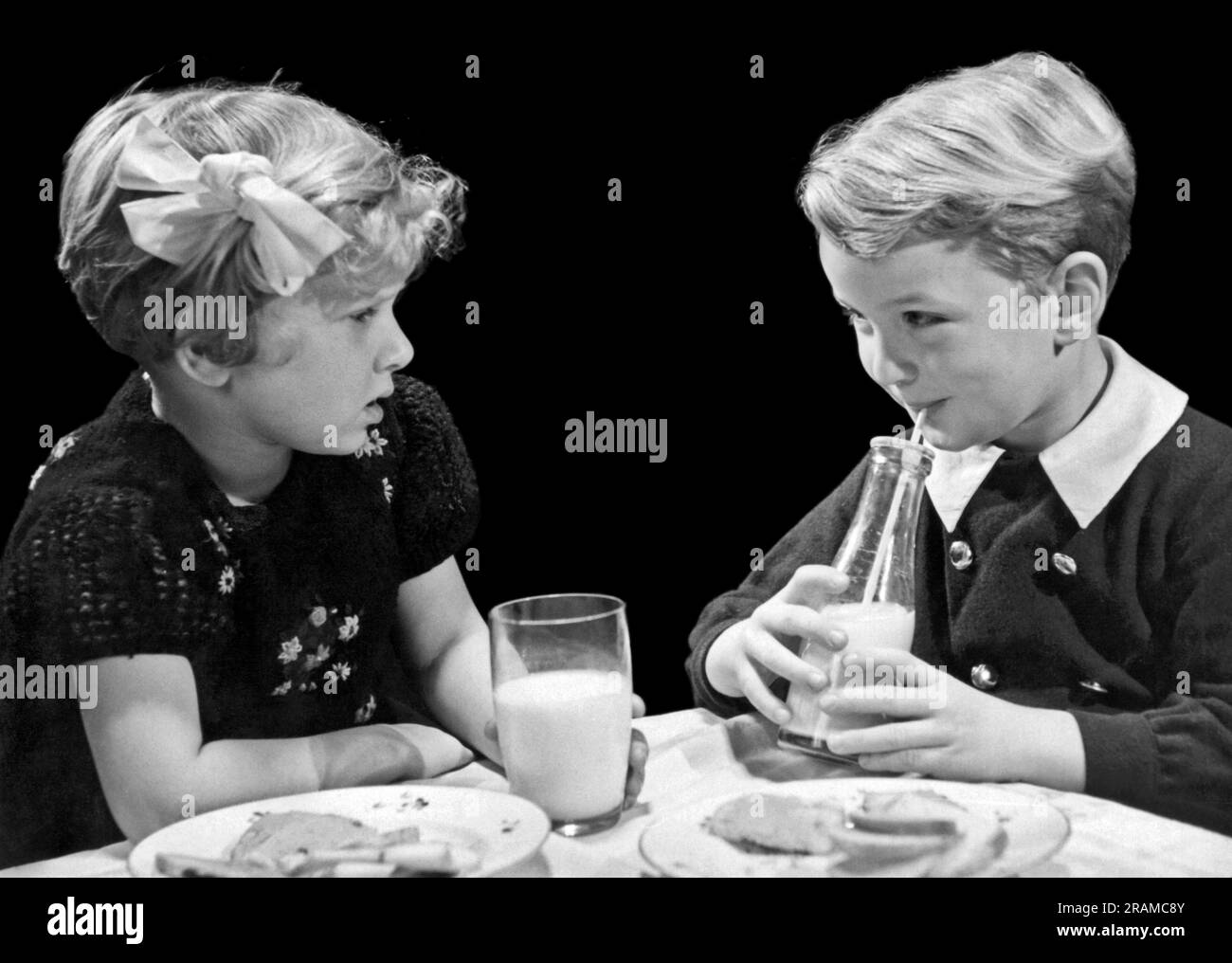 Vereinigte Staaten: c. 1940. Ein Junge und ein Mädchen schauen sich an, während sie Milch am Esstisch trinken. Stockfoto