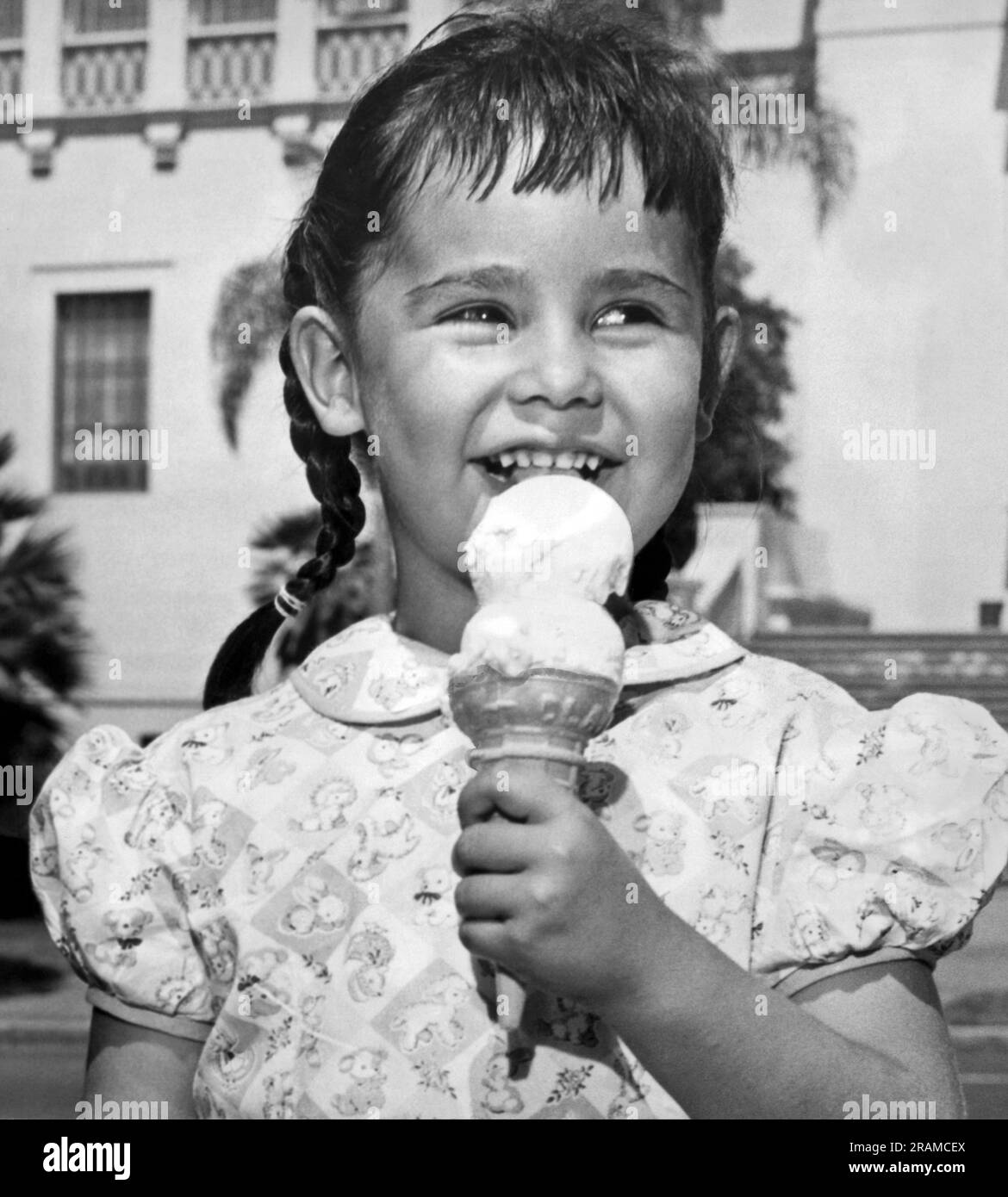 Kalifornien: ca. 1948. Ein lächelndes, junges Mädchen mit Zöpfen isst an einem warmen Sommertag gerne ein Doppel-Dip-Eis. Stockfoto