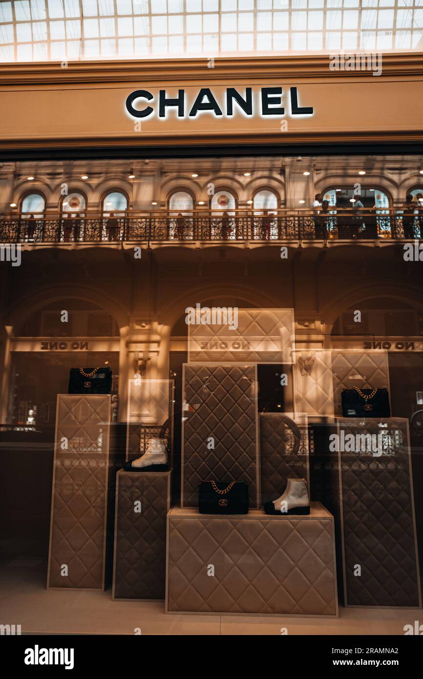 Eleganter, ästhetischer Eingang der Chanel Boutique. Neutraler beigefarbener Stand mit schwarzer Handtasche und weißen Schuhen im Schaufenster eines Luxusgeschäfts. Modemarke Stockfoto