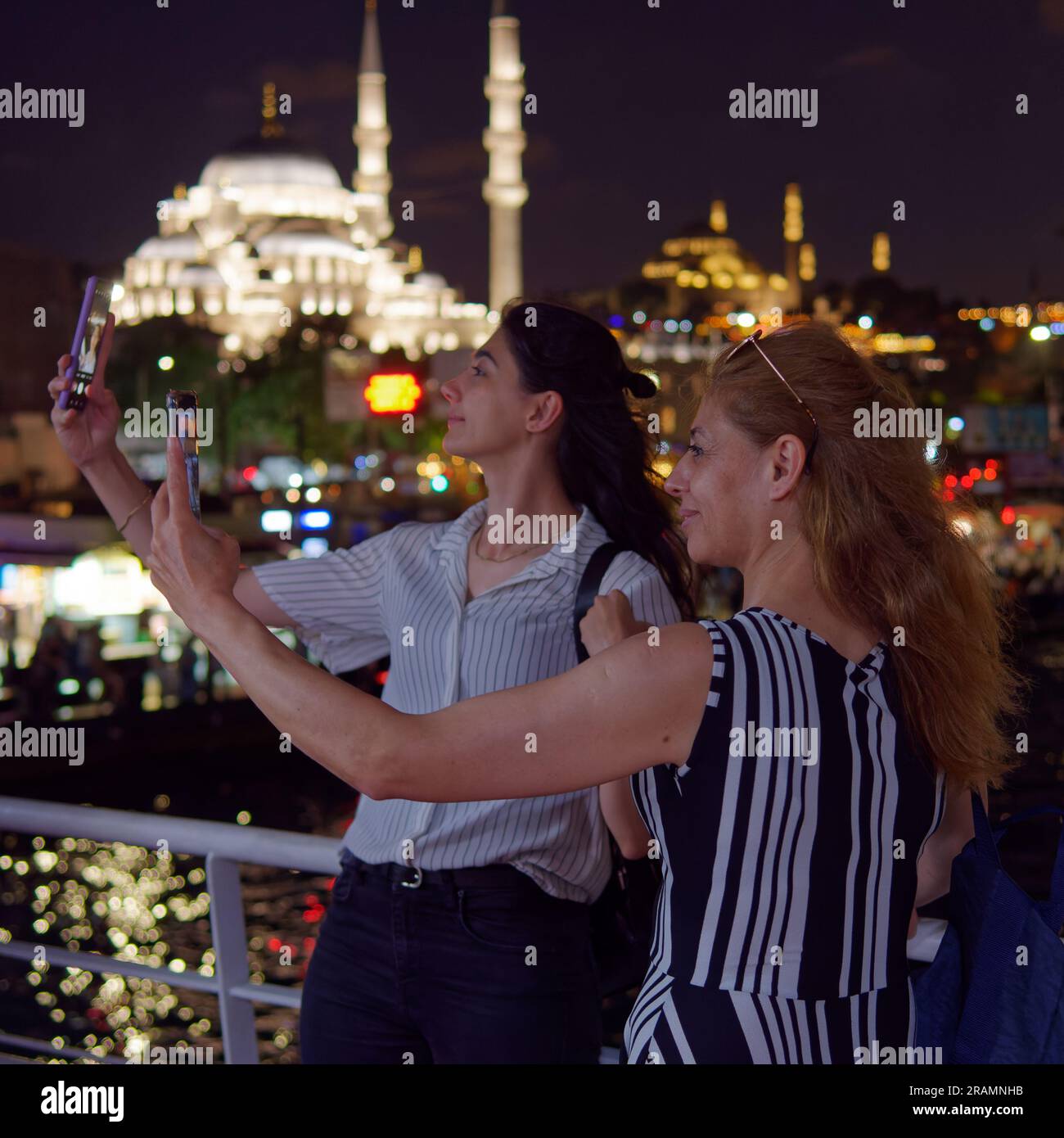 Zwei Frauen, Mutter und Tochter, nehmen nachts Selfies von einer Passagierfähre in Istanbul mit einer Moschee im Hintergrund. Stockfoto