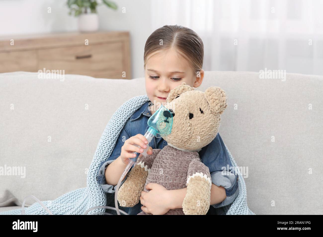 Kleines Mädchen mit Spielzeugbär und Vernebler zum Einatmen auf dem Sofa zu Hause Stockfoto