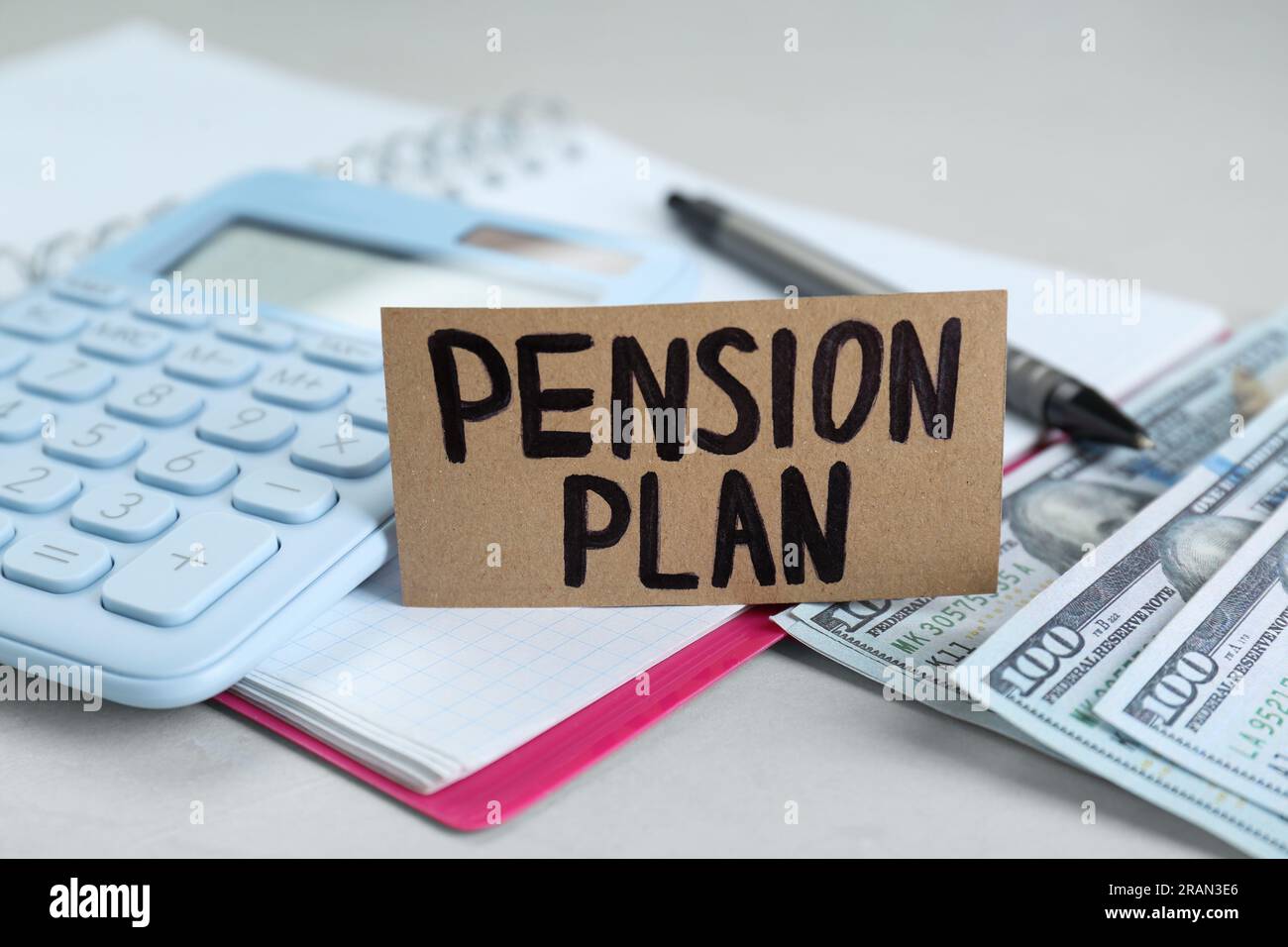 Karte mit Worten Pensionsplan, Banknoten, Taschenrechner und Notizbuch auf weißem Tisch, Nahaufnahme Stockfoto
