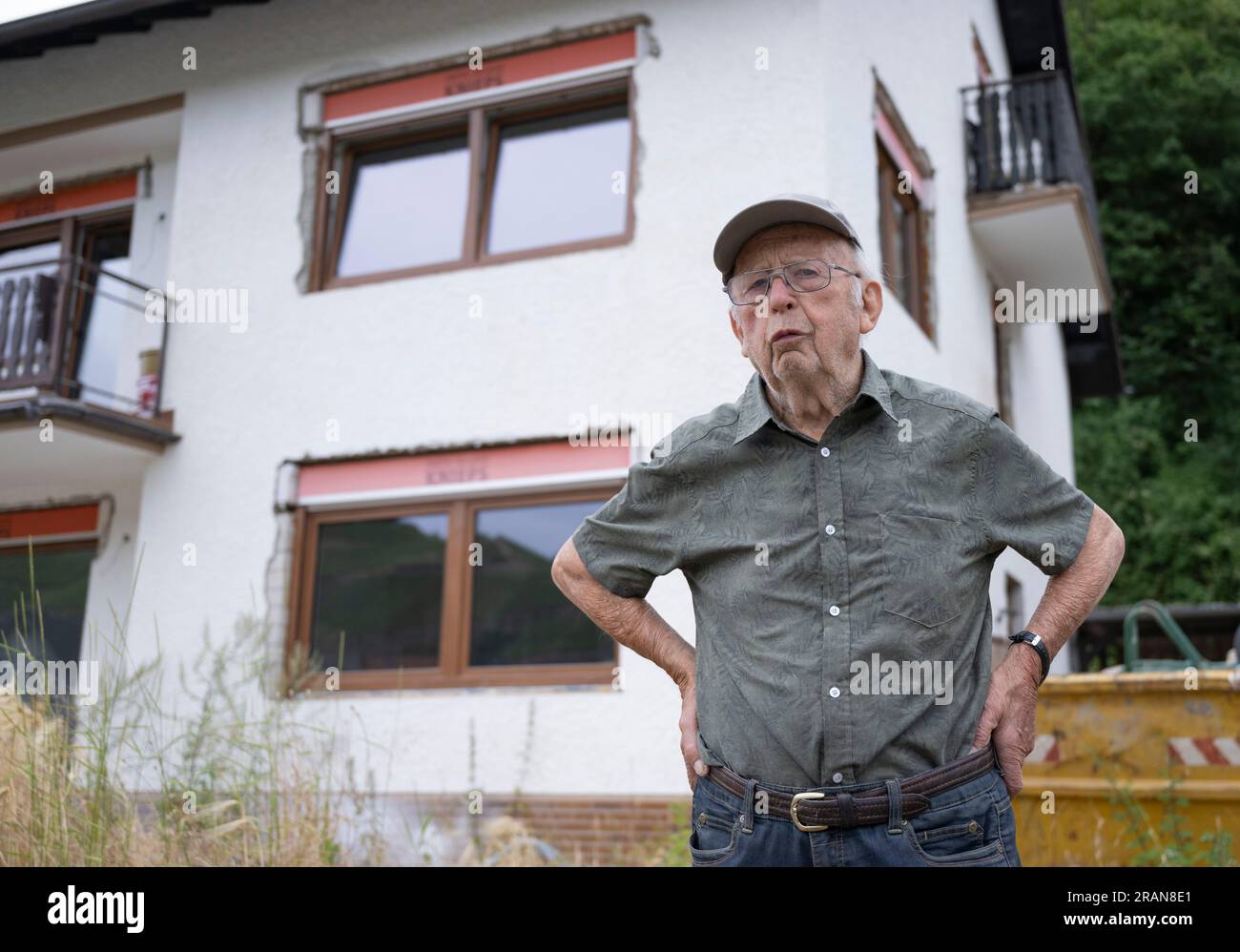 PRODUKTION - 28. Juni 2023, Rheinland-Pfalz, Dernau: Der 90-jährige Franz Kluckert steht vor seinem Haus am Ufer der Ahr. Als die Flutwelle kam, konnten sich der Seniorenbürger und seine Frau in letzter Minute im oberen Stockwerk retten. Jetzt hofft er, bald wieder in sein Haus einziehen zu können. Zwei Jahre nach der tödlichen Flutwelle stehen im Ahr-Tal noch mehrere völlig zerstörte Häuser. Gleichzeitig werden an vielen Stellen Bauarbeiten durchgeführt. Das Leben kehrt zurück - aber langsam. (Zu dpa: 'Gerüste und Ruinen: Rekonstruktion im Ahr-Tal Stockfoto