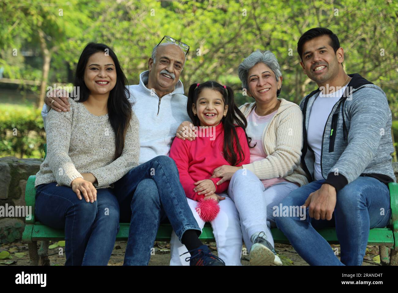 Glückliche Familie, die eine gute und fröhliche Zeit hat, auf einer Bank im grünen Park inmitten einer ruhigen Atmosphäre und einer frischen Luft-Umgebung zu sitzen. Kein Verschmutzungstag. Stockfoto
