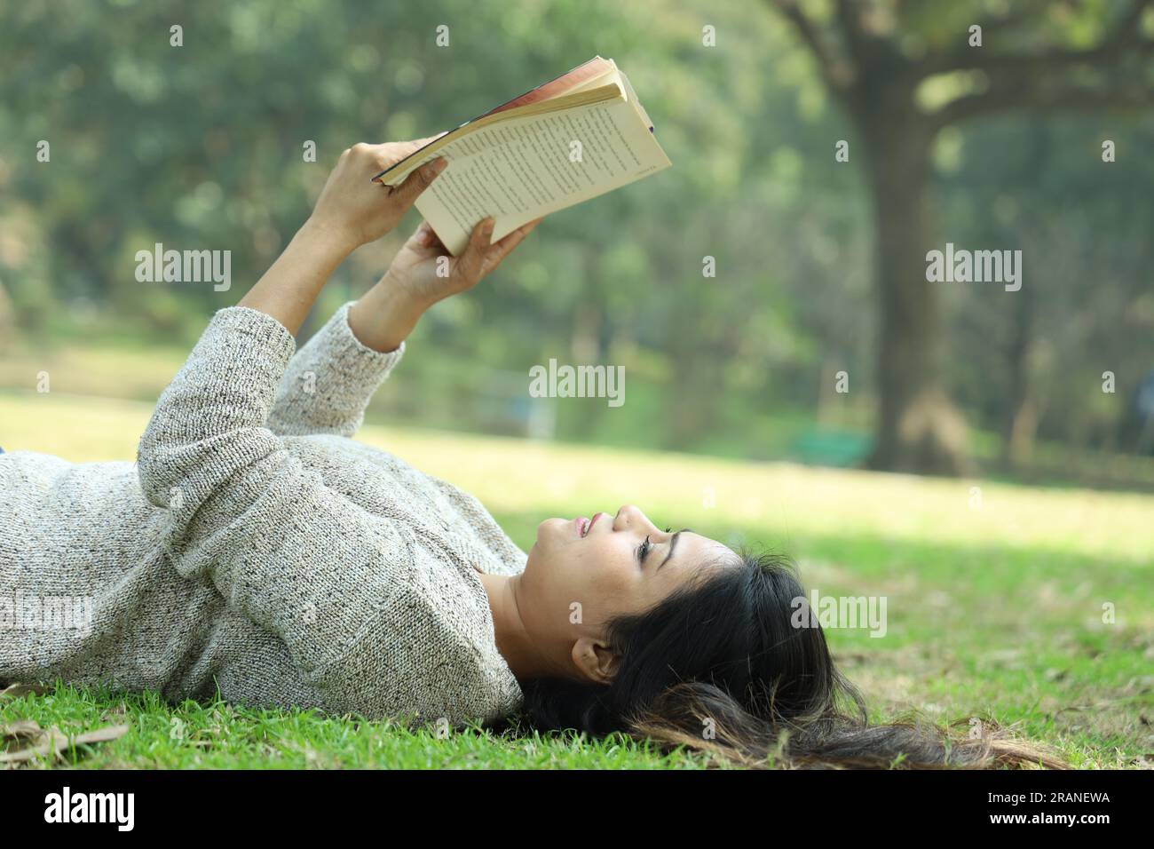 Ein hübsches College-Mädchen, das ein Buch liest, das im Gras liegt an einem Tag. Grüne, ruhige Umgebung Stockfoto