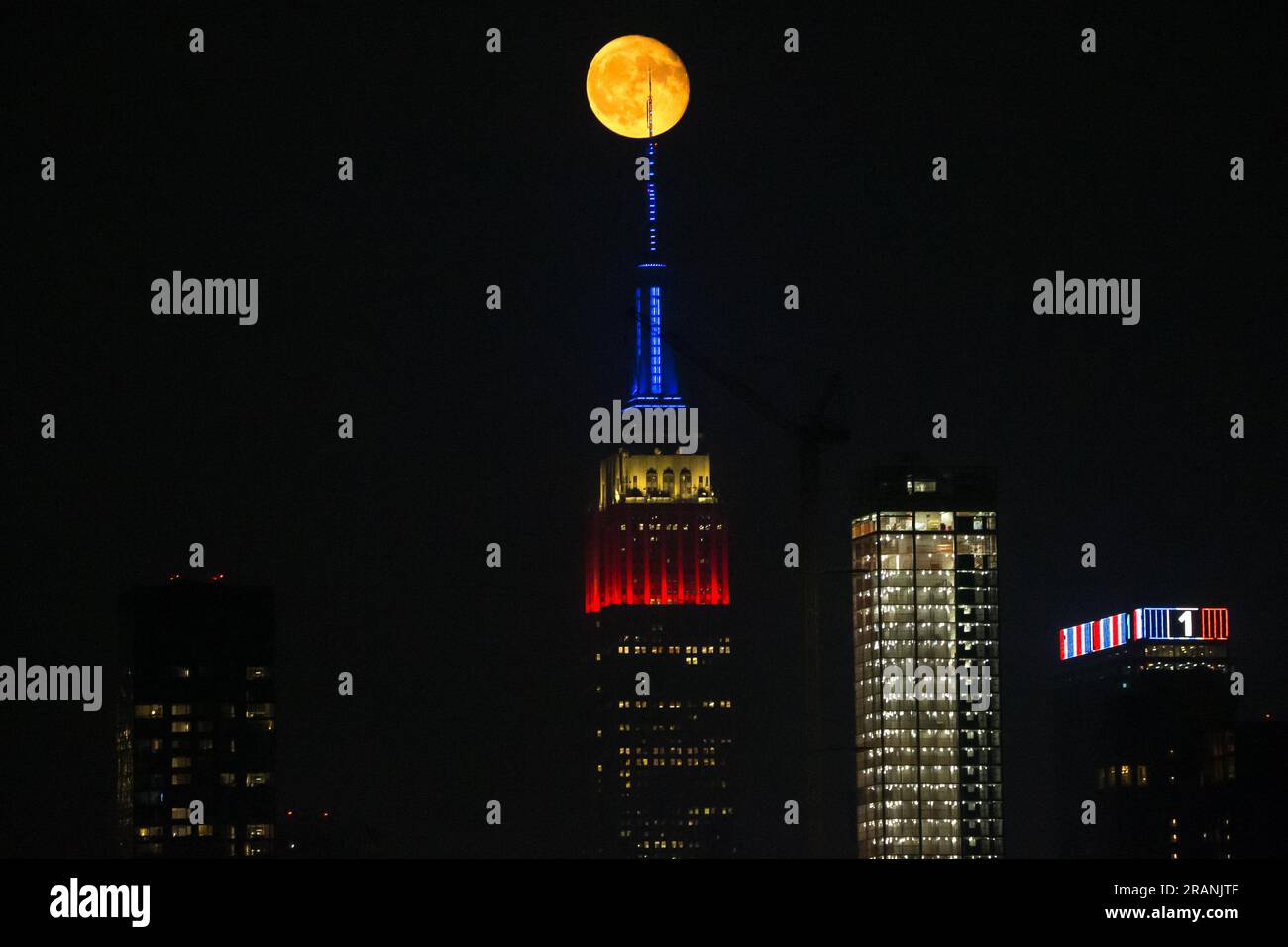 New York City, Usa. 04/07/2023, Vollmond erhebt sich hinter dem Empire State Building, das zu Ehren des Unabhängigkeitstages am 4. Juli in New York City, USA, in den Farben der amerikanischen Flagge erleuchtet ist. Kredit: Brasilien Photo Press/Alamy Live News Stockfoto