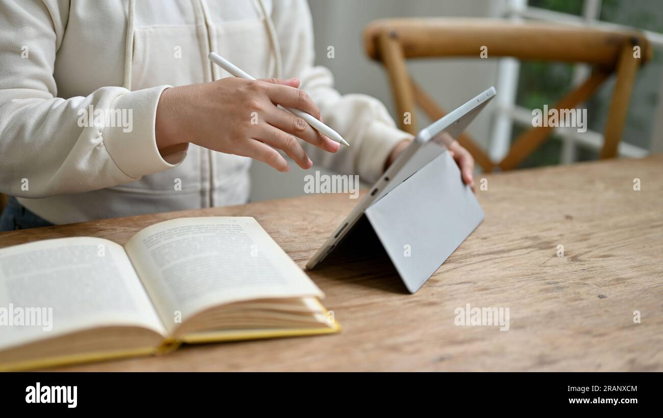 Nahaufnahme einer Frau in einem weißen Pullover, die ihr digitales Tablet verwendet, um ihre Aufgaben zu verwalten, während sie in einem Café arbeitet. Stockfoto