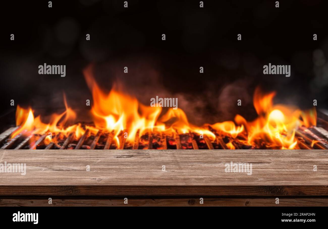 Barbecue-Grill mit brennendem Kamin und Holzkohle auf schwarzem Hintergrund, Holztisch Stockfoto