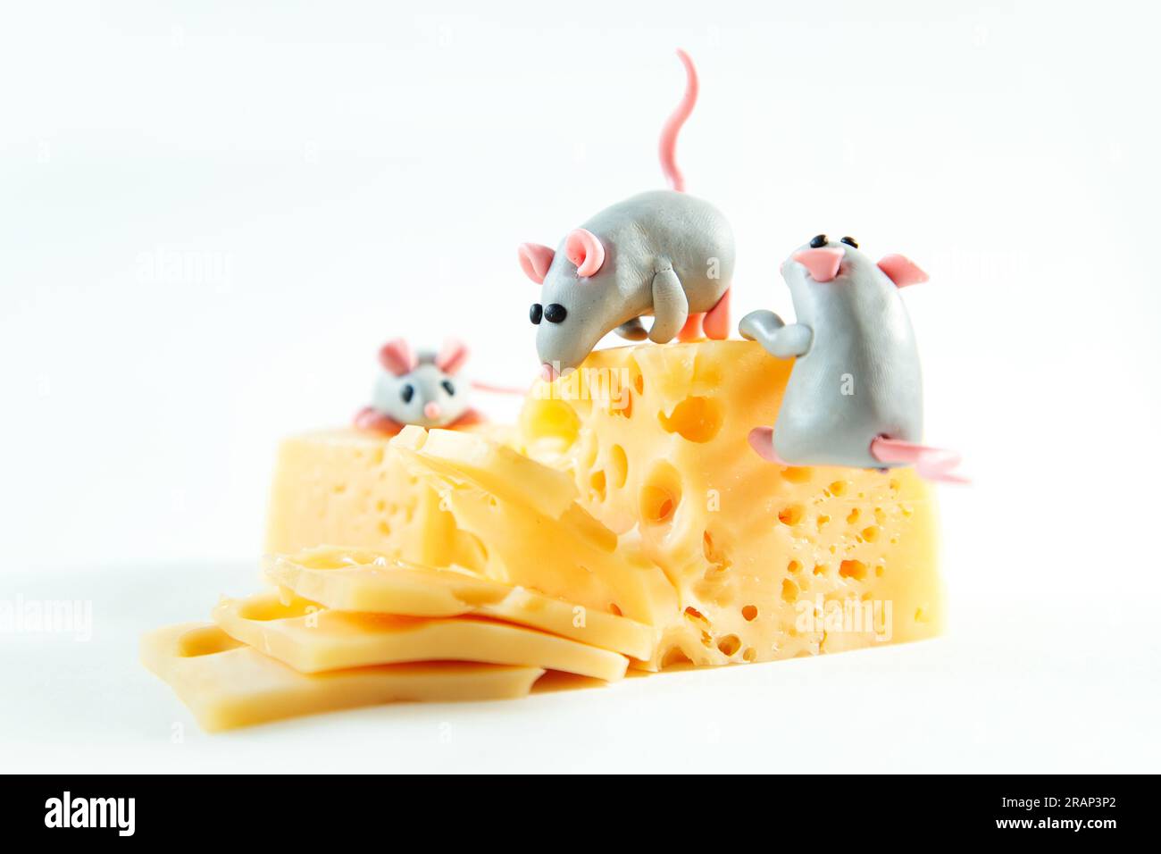 Kleine Plastikmäuse und ein Stück Käse mit Löchern. Weißer Hintergrund. Stockfoto