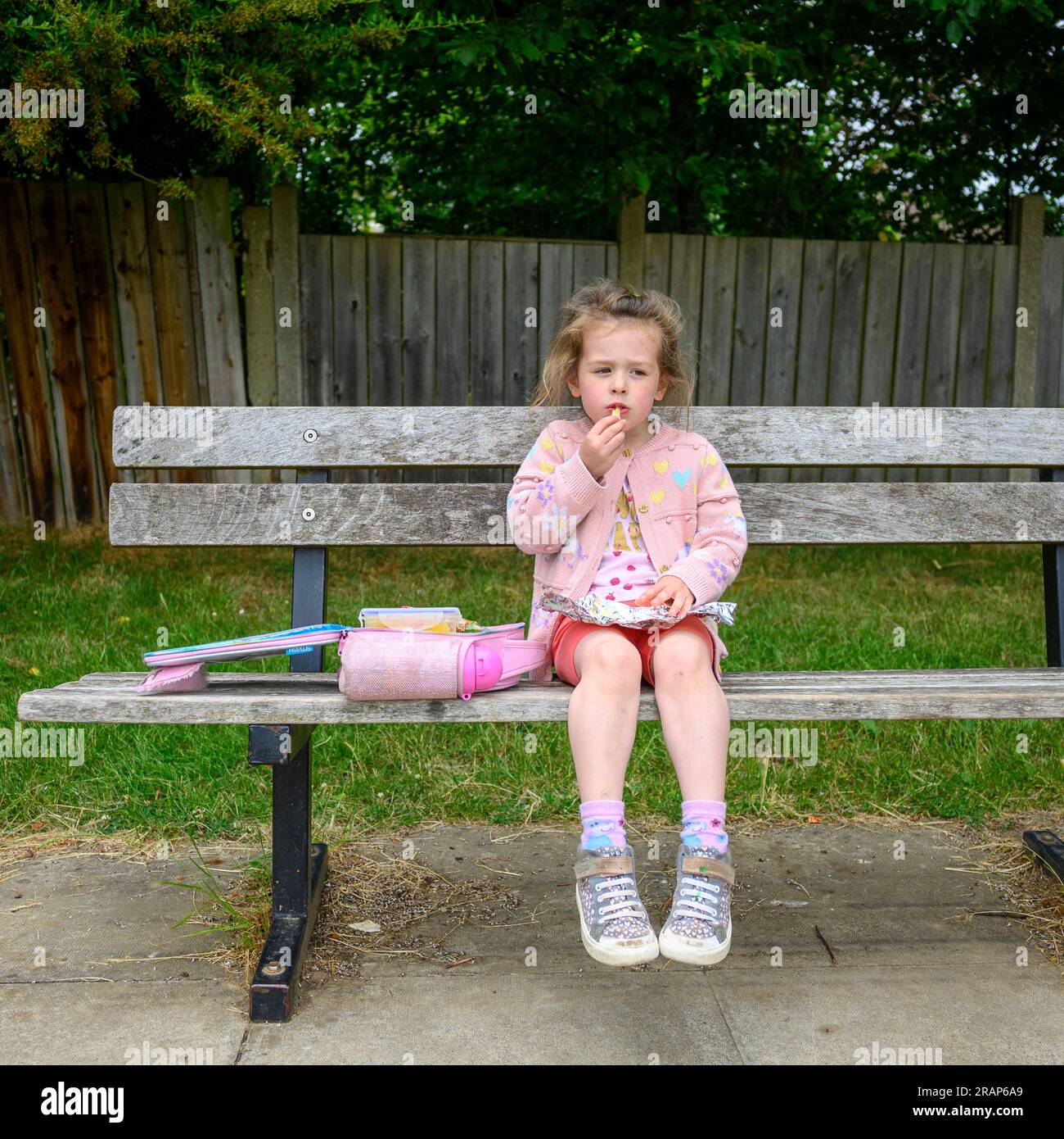 Ein Mädchen, das auf einer Parkbank sitzt und ein Lunchpaket isst Stockfoto