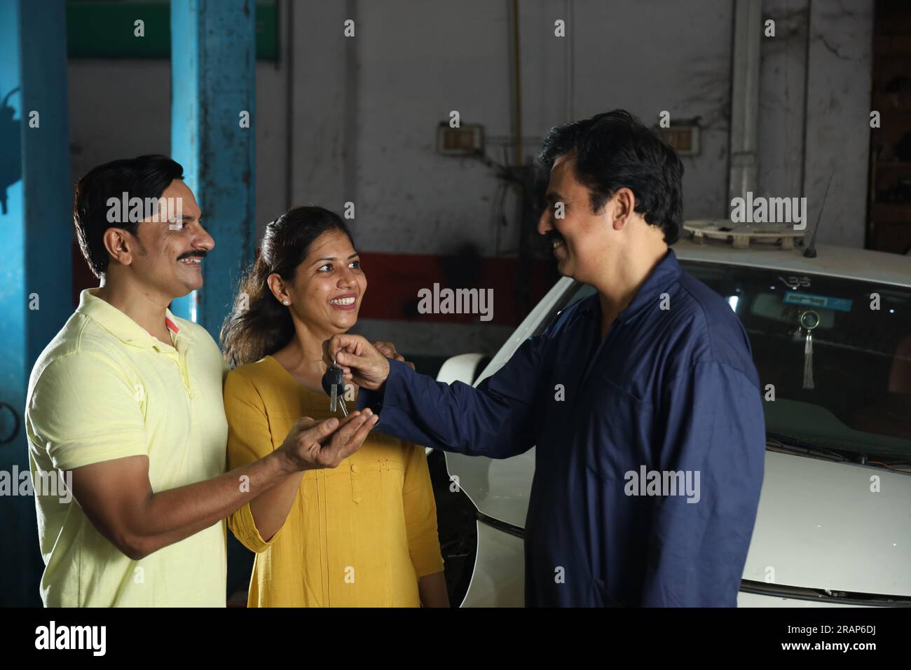 Indischer Automechaniker, der die Autoschlüssel an zufriedene Kunden liefert. Die Zufriedenheit der Kunden mit der ganzen Szene zu verdeutlichen, der fröhliche Autospezialist Stockfoto