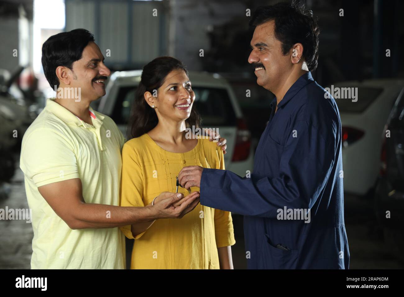 Indischer Automechaniker, der die Autoschlüssel an zufriedene Kunden liefert. Die Zufriedenheit der Kunden mit der ganzen Szene zu verdeutlichen, der fröhliche Autospezialist Stockfoto