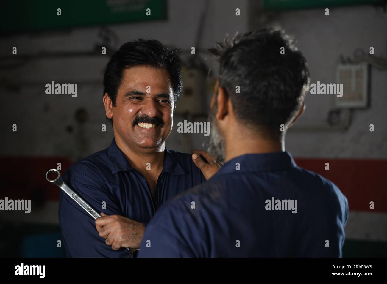 Porträt glücklicher indischer Automechaniker, die in der Tankstelle zusammenstehen. Autospezialisten, die Reparaturwerkzeuge für Autos halten. Professionelle Handwerker Stockfoto