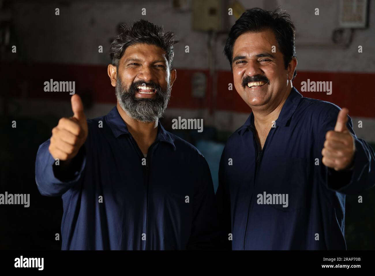 Porträt glücklicher indischer Automechaniker, die in der Tankstelle zusammenstehen. Autospezialisten, die Reparaturwerkzeuge für Autos halten. Professionelle Handwerker Stockfoto