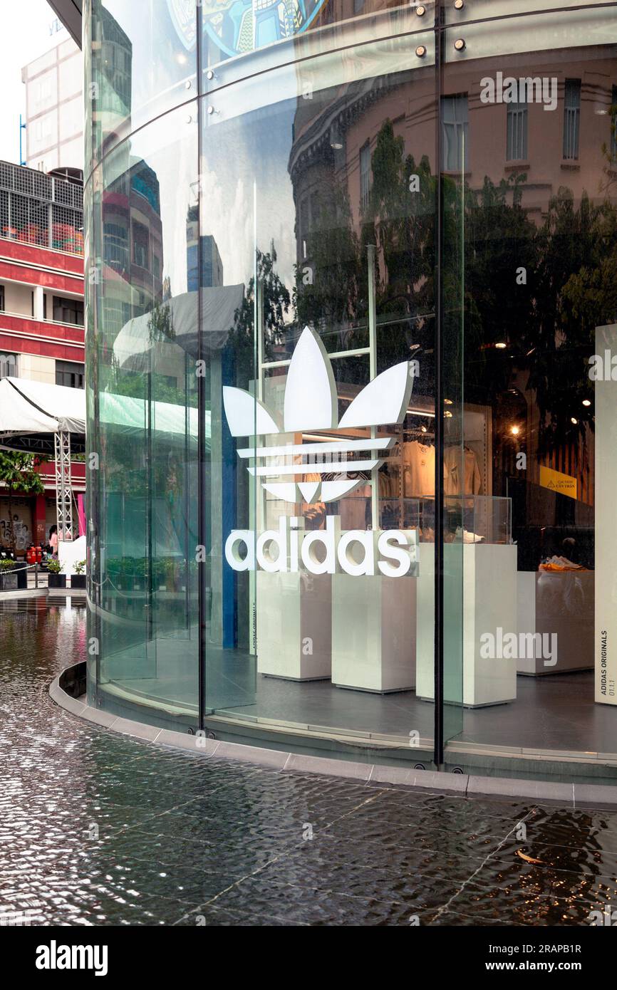 Ho-Chi-Minh-Stadt, Vietnam - 4. Juni 2023: Weißes Adidas-Logo auf einem Schaufenster eines Sportkleidergeschäfts. Berühmte Schuhfirma Werbung auf einem Glas im Einkaufszentrum Stockfoto